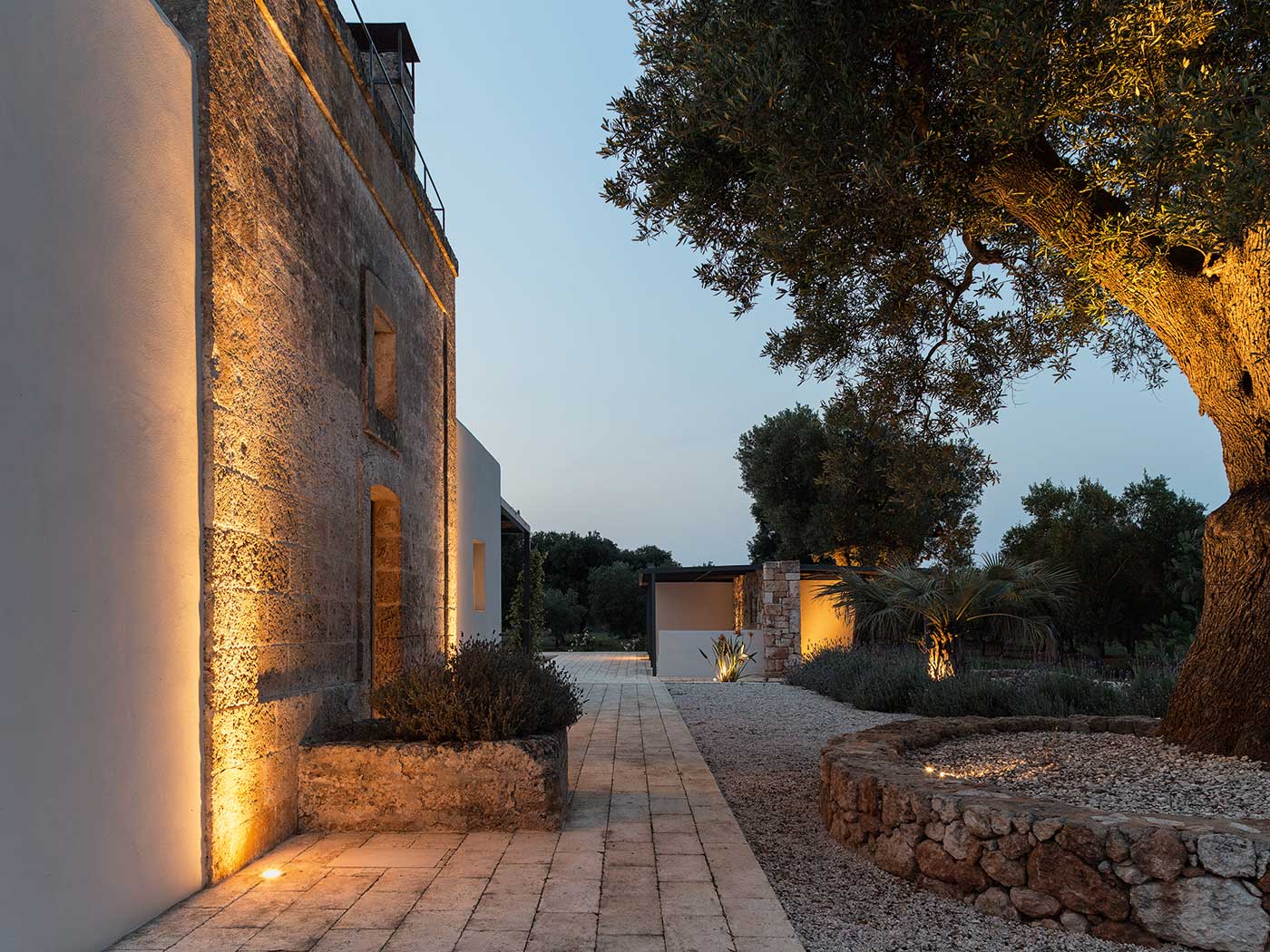 A restored residence in Brindisi finds its evening character in rough tuff and olive trees.