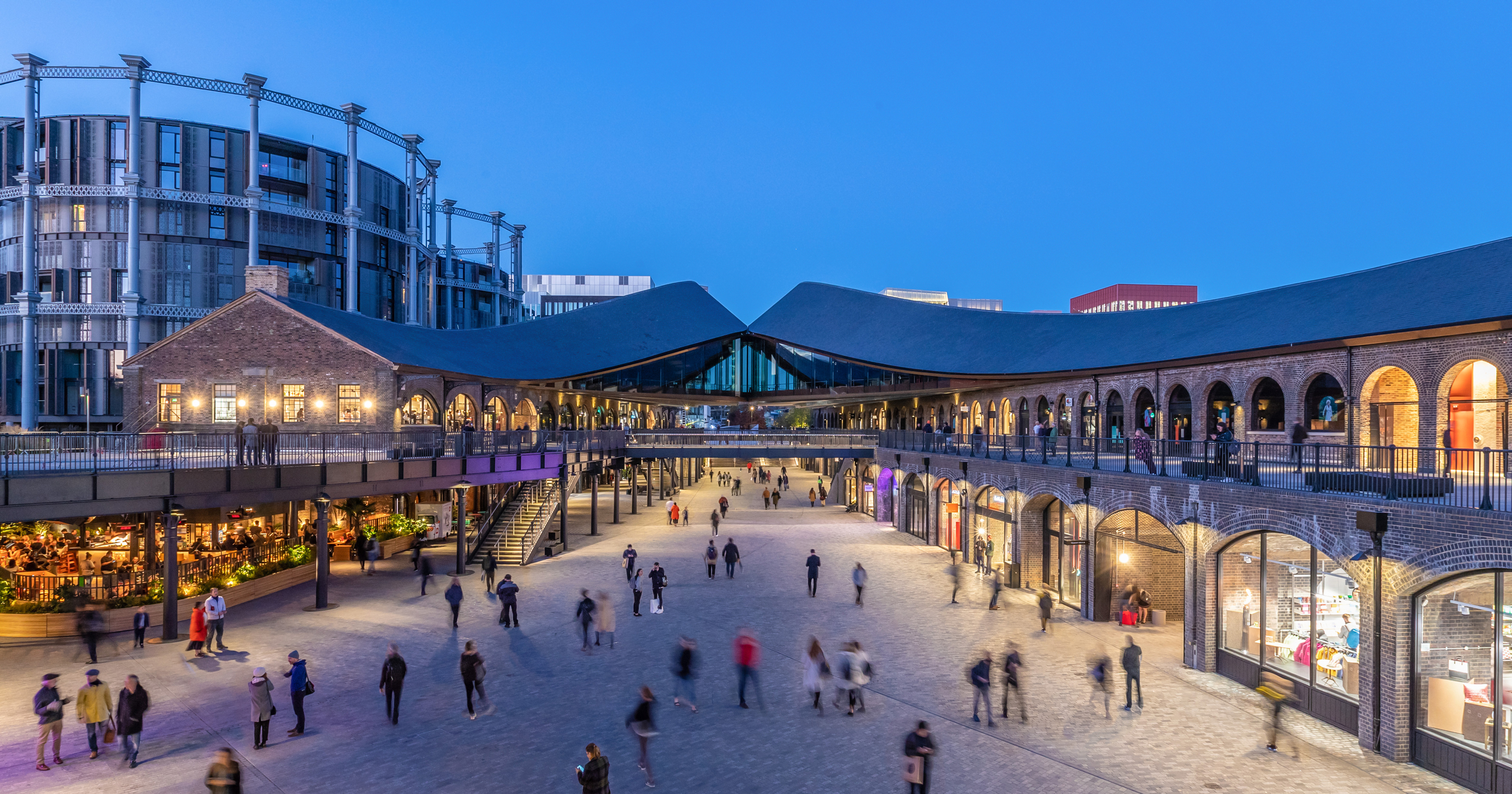 Coal Drops Yard carries warm light through a broad blue-hour scene.